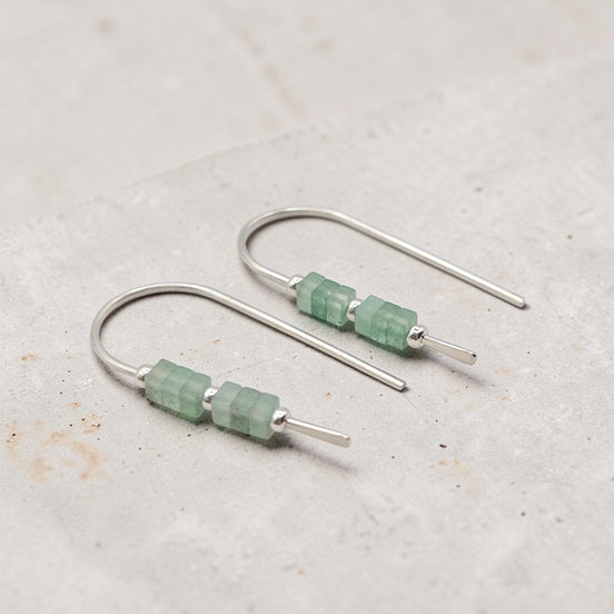 Silver earrings with green beads on a light gray background