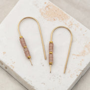 Pair of gold earrings with pink beads on a marble surface