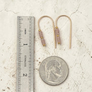 Gold earrings with brown beads next to a ruler and quarter for scale on a textured surface
