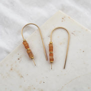 Pair of gold earrings with brown beads on a marble surface