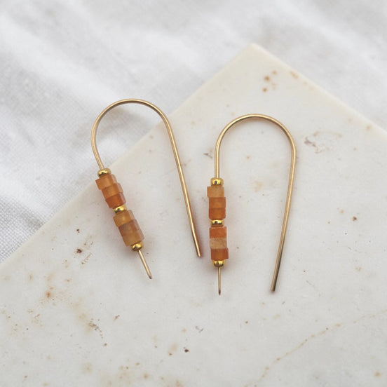 Pair of gold earrings with brown beads on a marble surface