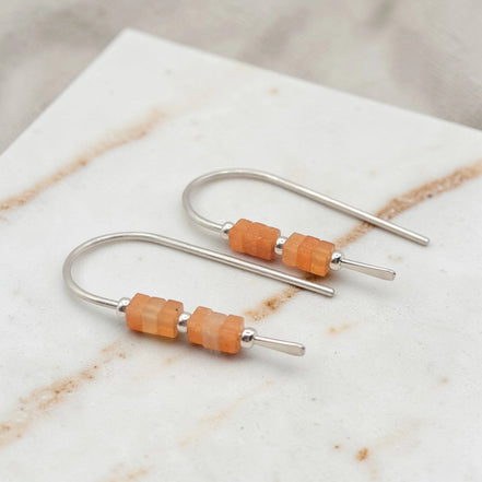 Pair of earrings with orange beads on a marble surface