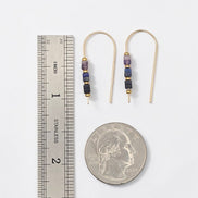 Pair of beaded earrings with a ruler and quarter for scale on a white background