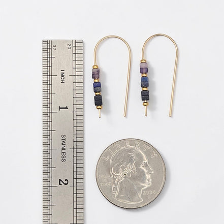 Pair of beaded earrings with a ruler and quarter for scale on a white background