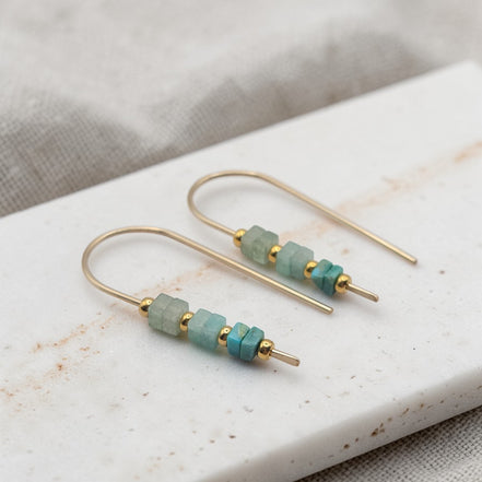 Gold earrings with green beads on a marble surface