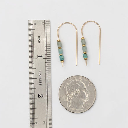 Pair of beaded earrings next to a ruler and a quarter for scale on a white background