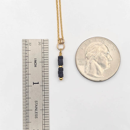 Gold necklace with black beads next to a ruler and quarter for scale on a white background