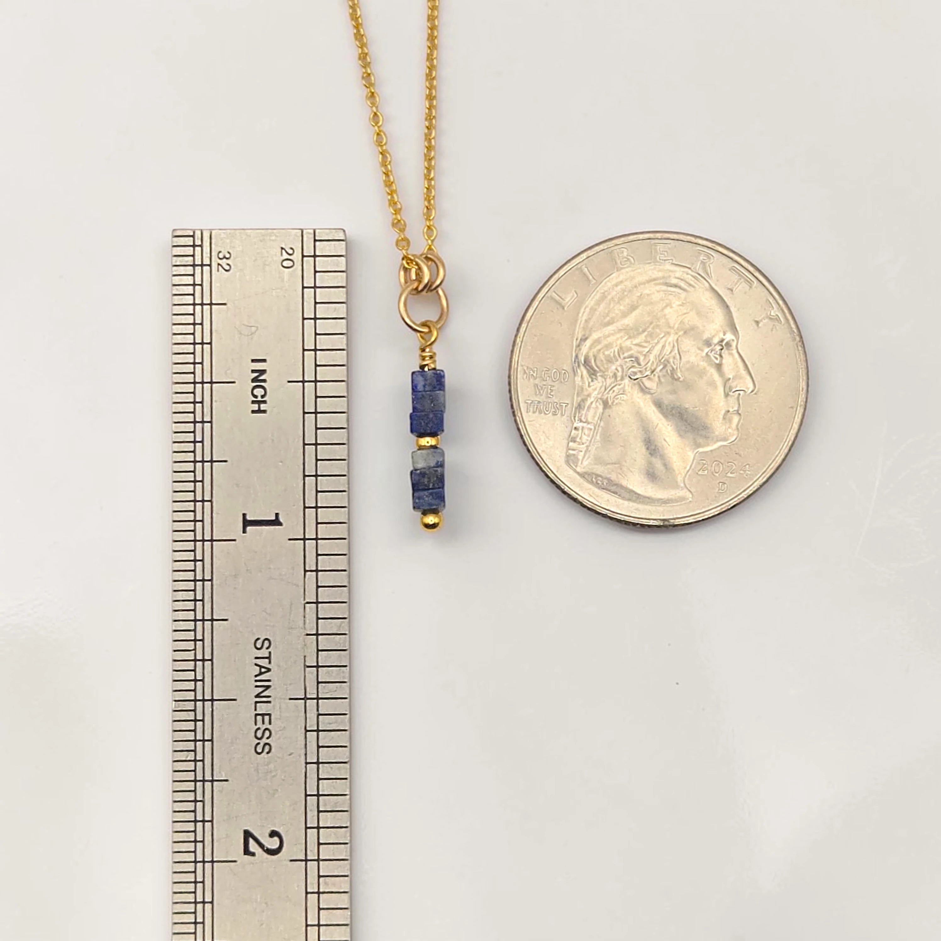Gold necklace with blue beads next to a ruler and quarter for scale on a white background