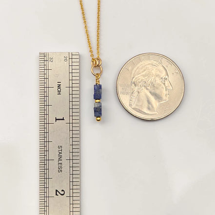 Gold necklace with blue beads next to a ruler and quarter for scale on a white background