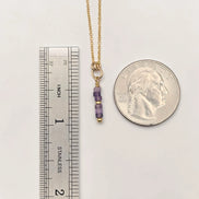 Gold necklace with purple beads next to a ruler and a quarter for scale on a white background