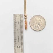 Gold necklace with beads next to a ruler and a quarter for scale on a white background