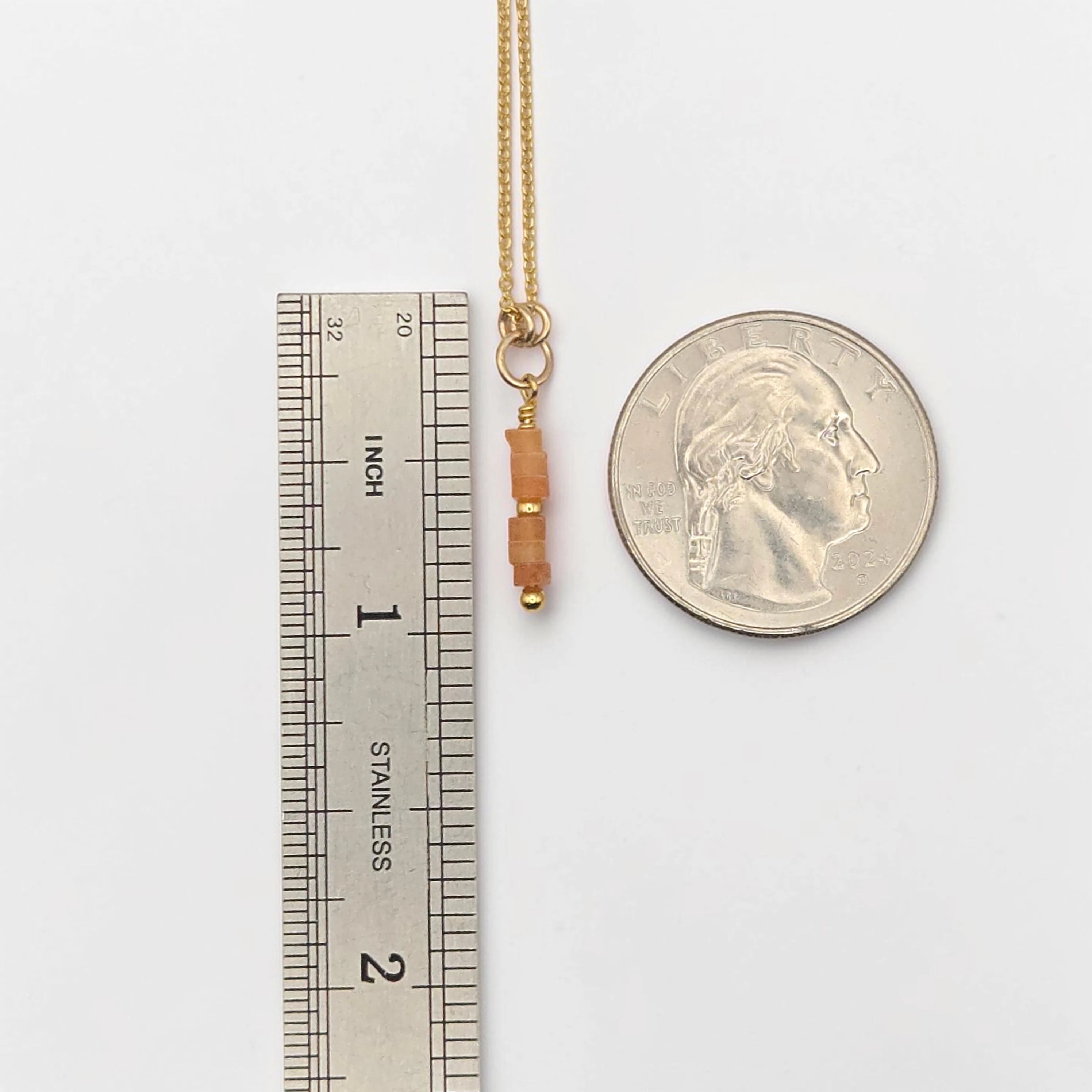 Gold necklace with beads next to a ruler and a quarter for scale on a white background