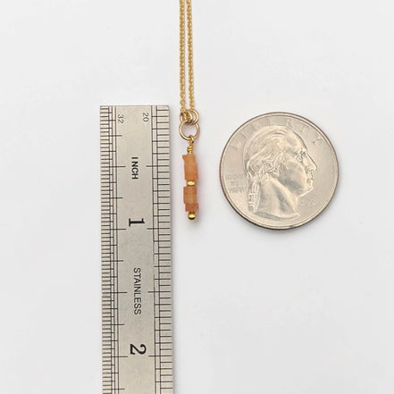 Gold necklace with beads next to a ruler and a quarter for scale on a white background