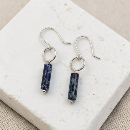 Silver earrings with blue cylindrical beads on a white stone surface