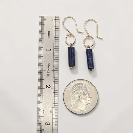 Pair of gold earrings with blue beads next to a ruler and quarter for scale on a white background