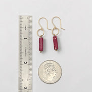 Gold earrings with red beads next to a ruler and quarter for scale on a white background