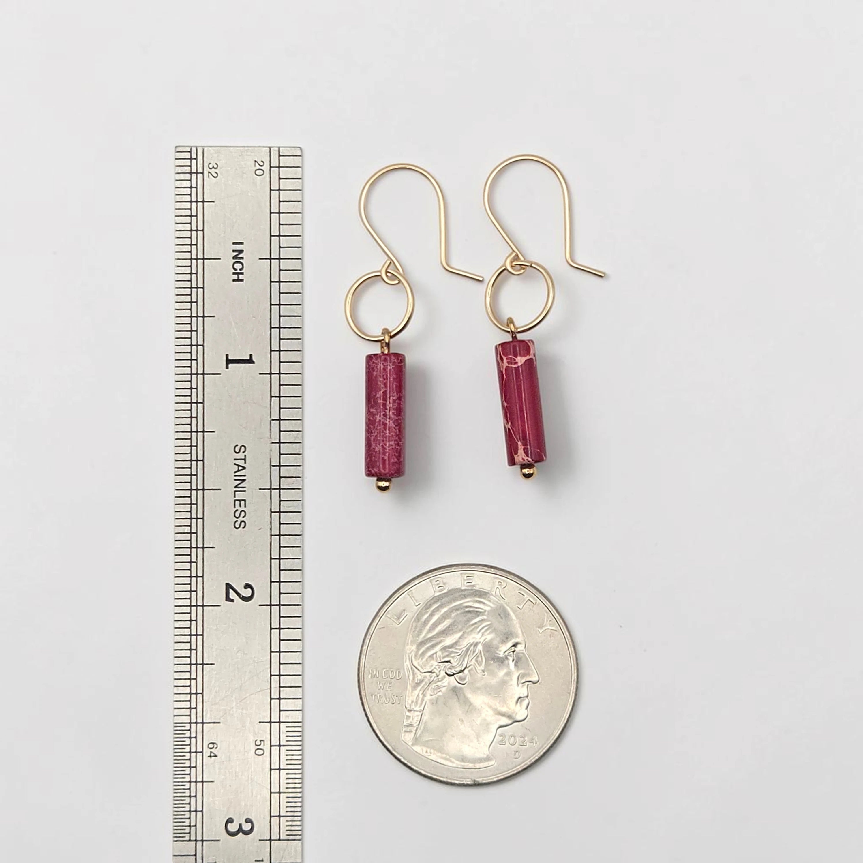 Gold earrings with red beads next to a ruler and quarter for scale on a white background