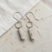 Silver earrings with cylindrical white stones on a marble surface