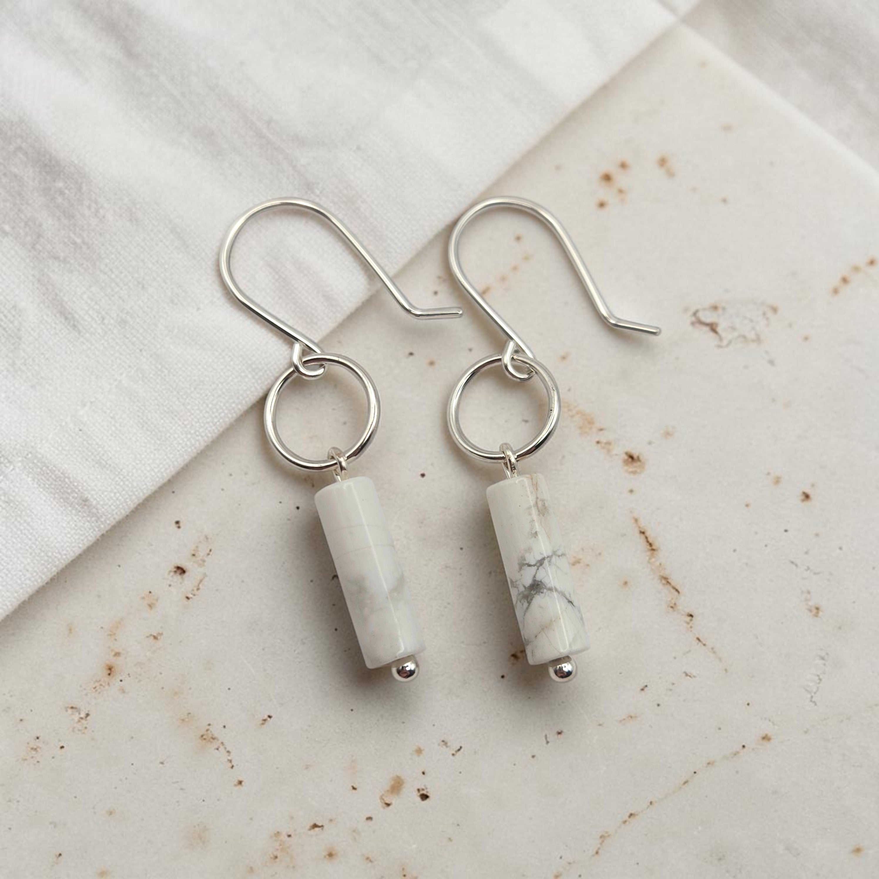 Silver earrings with cylindrical white stones on a marble surface
