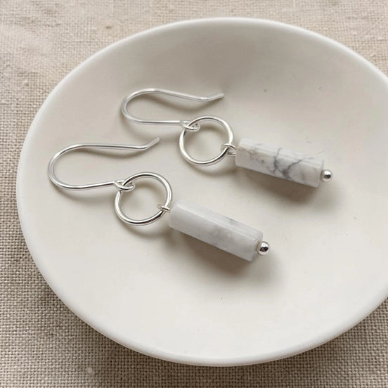 Pair of silver earrings with marble-like beads on a white dish.