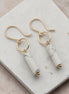 Gold earrings with white cylindrical stones on a marble surface