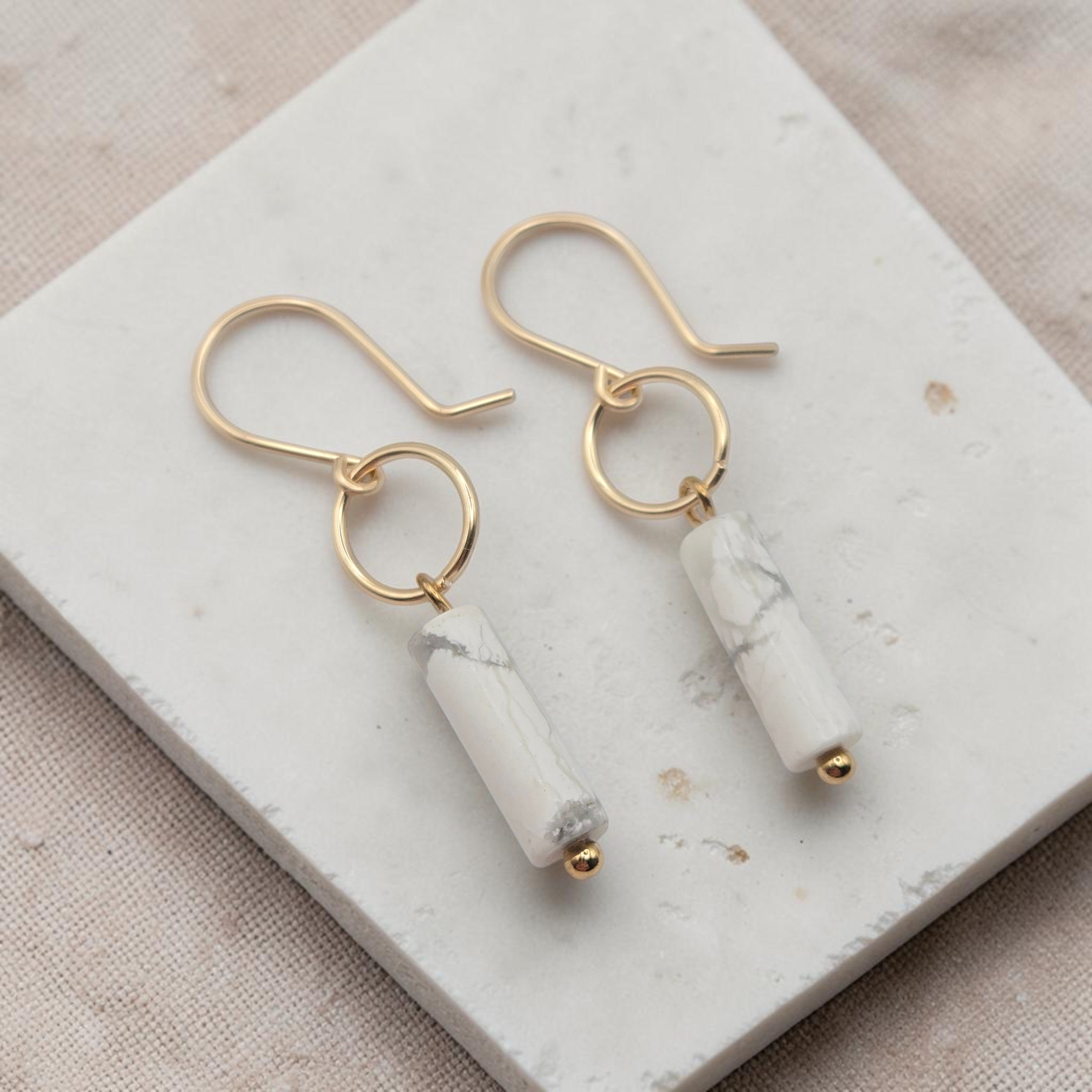 Gold earrings with white cylindrical stones on a marble surface