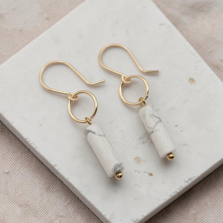 Gold earrings with white cylindrical stones on a marble surface