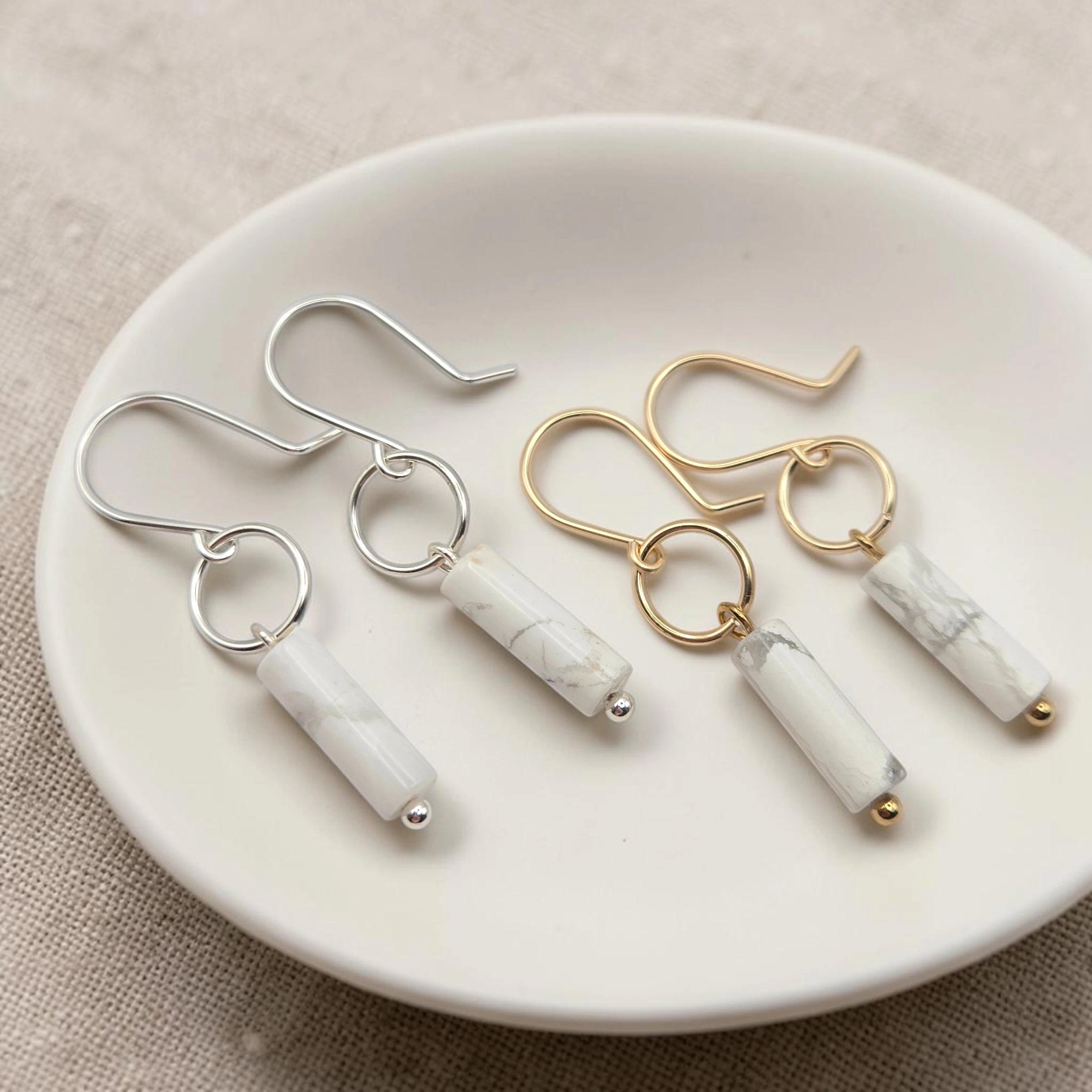 Pair of earrings with marble-like cylindrical pendants on a white plate.