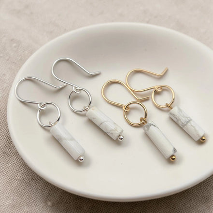 Pair of earrings with marble-like cylindrical pendants on a white plate.