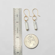 Gold earrings with cylindrical beads next to a ruler and quarter for scale on a light gray background