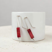 Red cylindrical earrings with silver hooks on a white surface