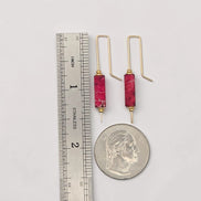 Gold earrings with red stones next to a ruler and quarter for scale on a white background
