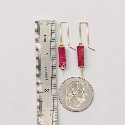 Gold earrings with red stones next to a ruler and quarter for scale on a white background