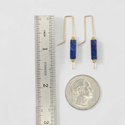 Pair of gold earrings with blue cylindrical stones next to a ruler and quarter for scale on a white background