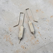 Pair of earrings with white cylindrical beads and silver hooks on a textured surface