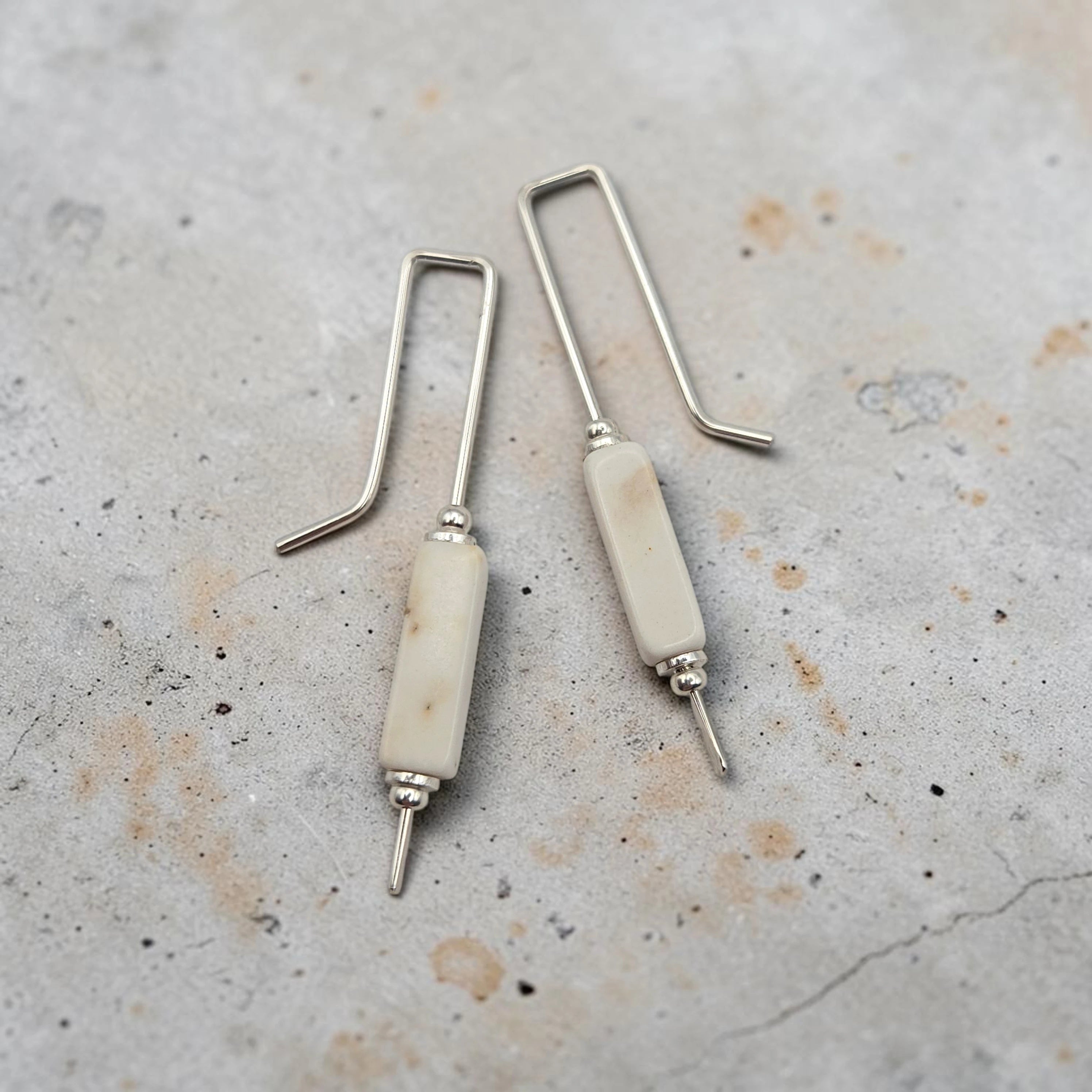 Pair of earrings with white cylindrical beads and silver hooks on a textured surface
