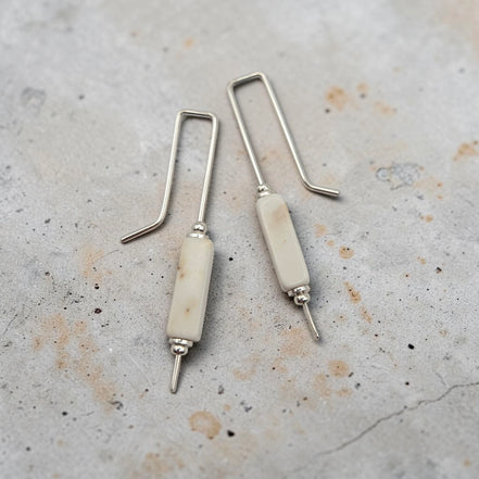 Pair of earrings with white cylindrical beads and silver hooks on a textured surface