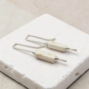Pair of earrings with white beads and silver hooks on a textured white surface.