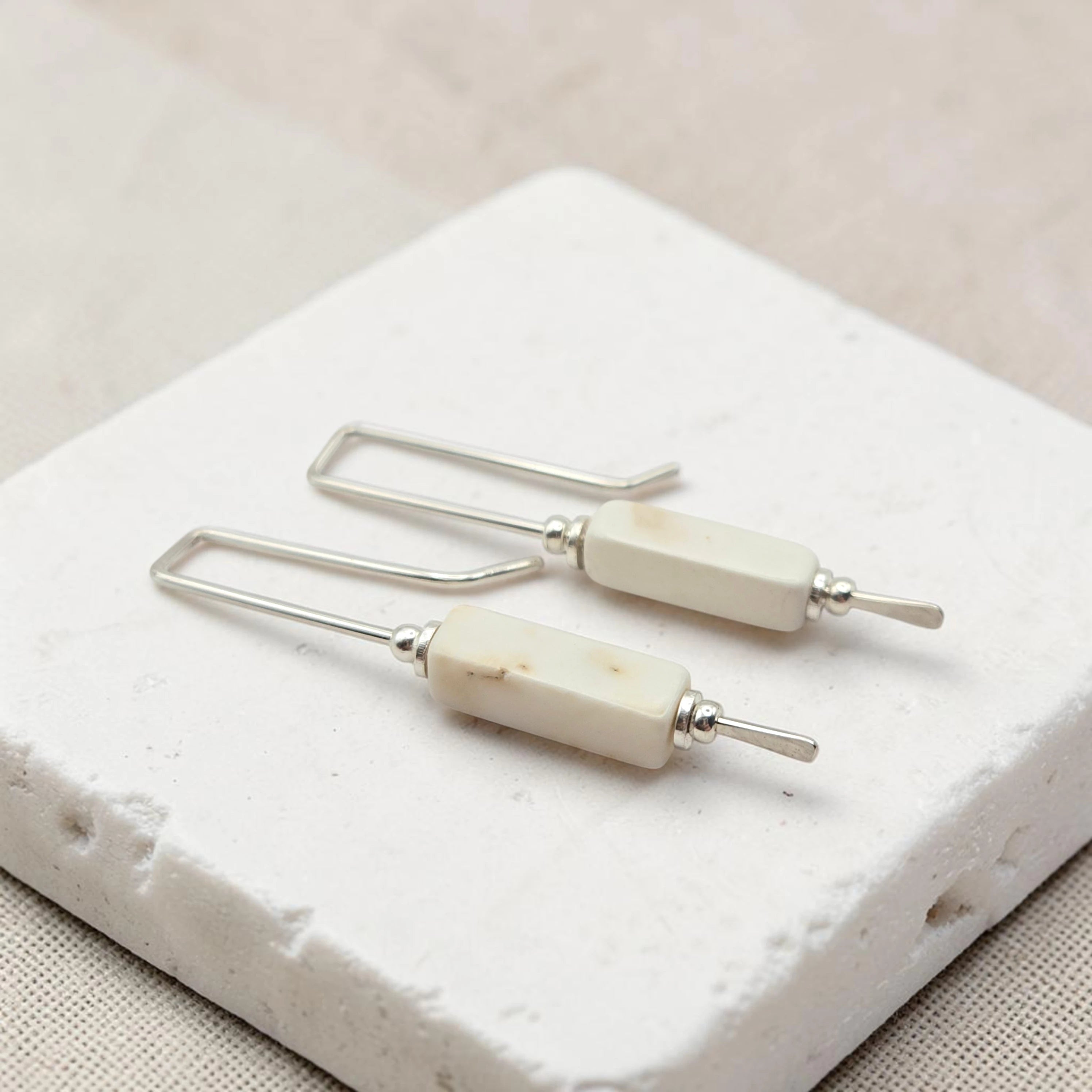 Pair of earrings with white beads and silver hooks on a textured white surface.