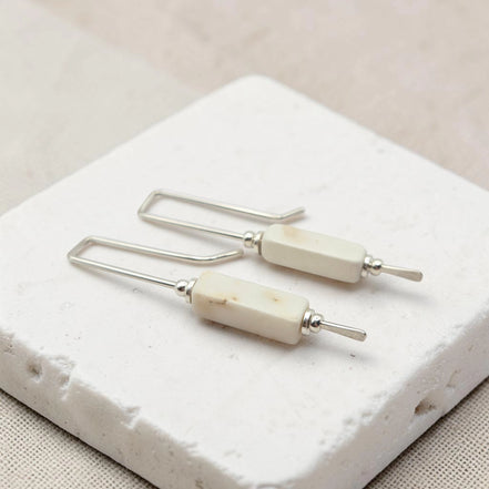 Pair of earrings with white beads and silver hooks on a textured white surface.