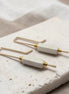Pair of earrings with gold and white components on a textured surface