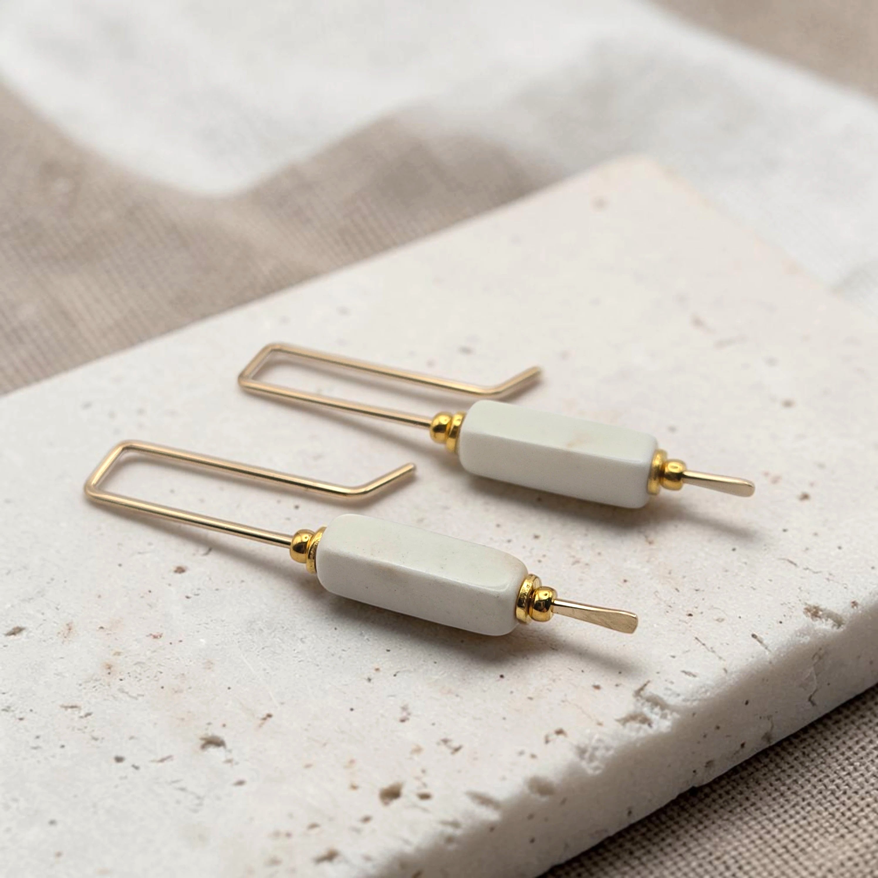 Pair of earrings with gold and white components on a textured surface