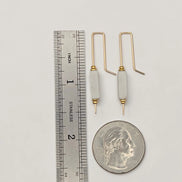 Two gold and white crochet hooks next to a ruler and a quarter for scale on a light gray background.