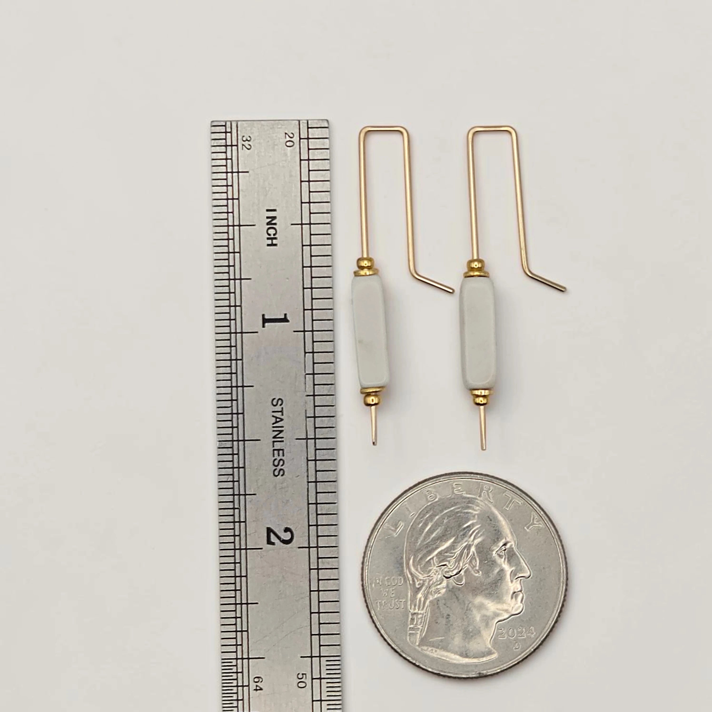Two gold and white crochet hooks next to a ruler and a quarter for scale on a light gray background.