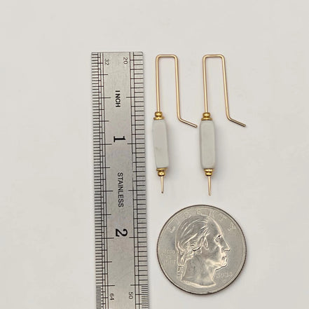 Two gold and white crochet hooks next to a ruler and a quarter for scale on a light gray background.