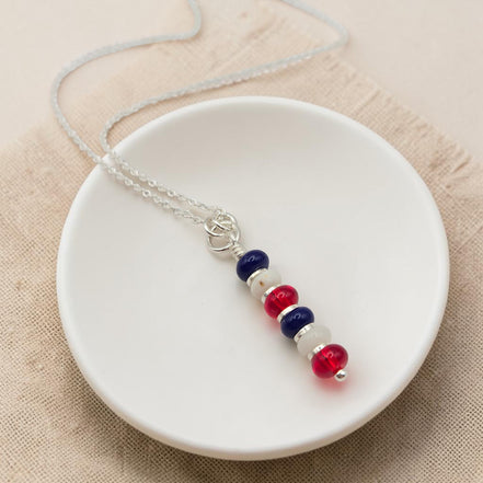 Necklace with red, white, and blue beads on a white dish against a beige background