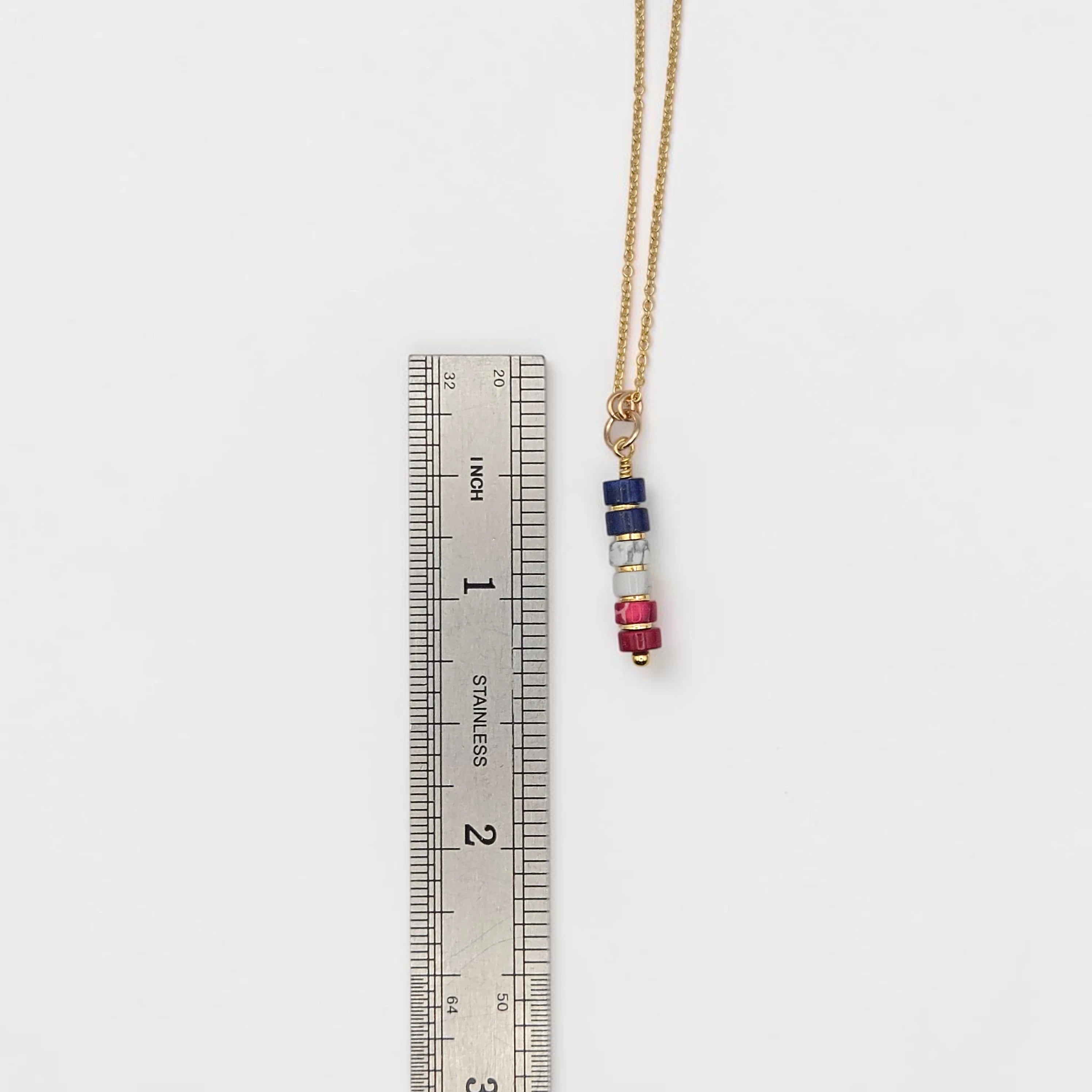 Necklace with colorful beads on a ruler for scale on a white background