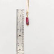 Necklace with a red pendant next to a ruler on a white background