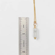 Gold necklace with a clear pendant next to a ruler on a white background