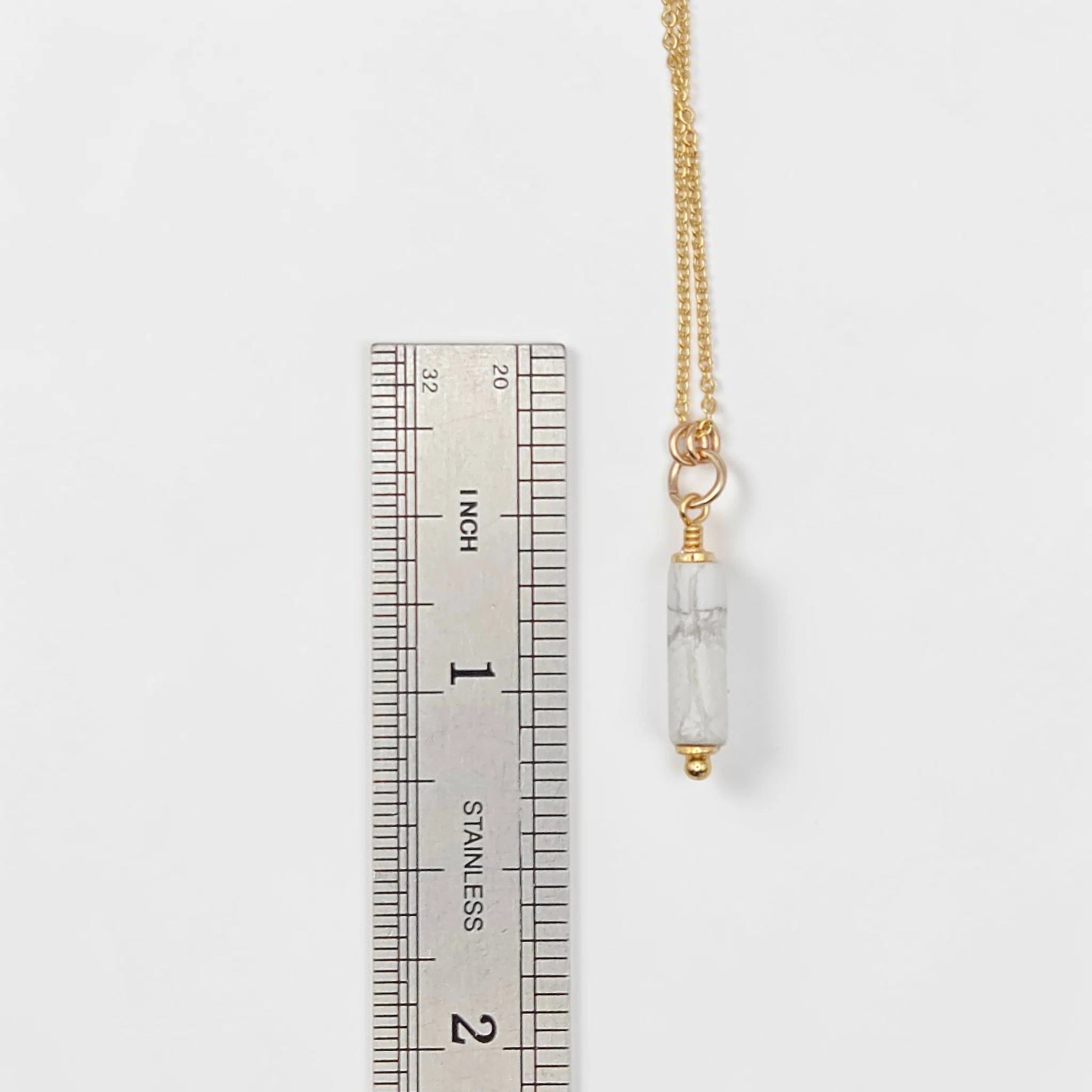 Gold necklace with a clear pendant next to a ruler on a white background